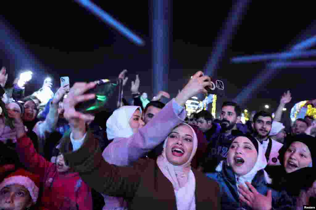 A woman uses a mobile phone as people gather during New Year's celebrations, after the ousting of Syria's Bashar al-Assad, in Damascus, Syria, Jan. 1, 2024. 