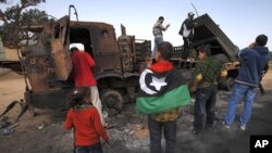 People look at weapons belonging to forces loyal to Libyan leader Muammar Gaddafi, destroyed by a coalition air strike, along a road between Benghazi and Ajdabiyah, March 23, 2011