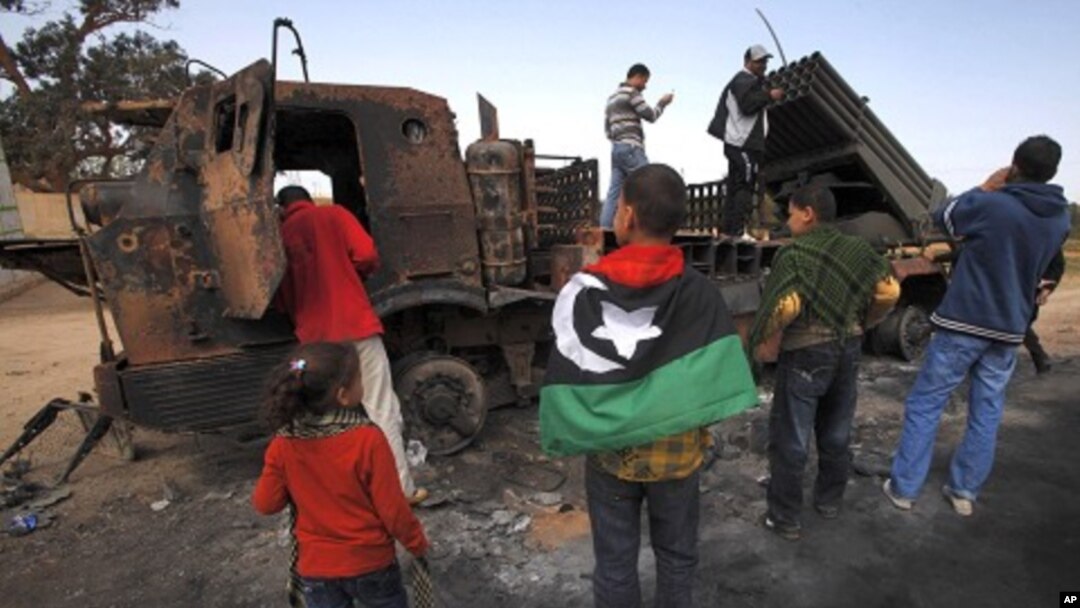 People look at weapons belonging to forces loyal to Libyan leader Muammar Gaddafi, destroyed by a coalition air strike, along a road between Benghazi and Ajdabiyah, March 23, 2011