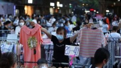 A vendor wearing a face mask following the coronavirus disease (COVID-19) outbreak holds clothing items for sale at a street stall on Jianghan Road in Wuhan, Hubei province, China June 8, 2020. Picture taken June 8, 2020. (China Daily via REUTERS)