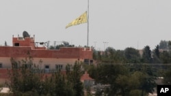 Pasukan Kurdi mengibarkan bendera di sebuah gedung di Tal Abyad, Suriah hari Selasa (16/6).