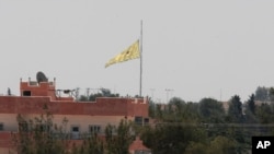 FILE - In this photo taken from the Turkish side of the border between Turkey and Syria, in Akcakale, southeastern Turkey, a flag of the Kurdish People's Protection Units, or YPG, flies over the town of Tal Abyad, Syria, June 16, 2015. 