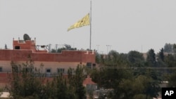 FILE - In this photo taken from the Turkish side of the border between Turkey and Syria, in Akcakale, southeastern Turkey, a flag of the Kurdish People's Protection Units, or YPG, flies over the town of Tal Abyad, Syria, June 16, 2015. 