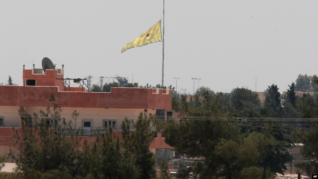 Pasukan Kurdi mengibarkan bendera di sebuah gedung di Tal Abyad, Suriah hari Selasa (16/6).