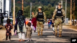 FILE - U.S. Military Police walk past Afghan refugees at the Fort McCoy U.S. Army base, Sept. 30, 2021, in Wisconsin. The fort is one of eight military installations that are temporarily housing Afghans who fled after the Taliban took over their country.