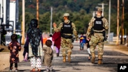 FILE - U.S. Military Police walk past Afghan refugees at the Fort McCoy U.S. Army base, in Wisconsin, Sept. 30, 2021. 