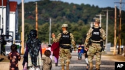 FILE - U.S. Military Police walk past Afghan refugees at the Fort McCoy U.S. Army base, Sept. 30, 2021, in Wisconsin.