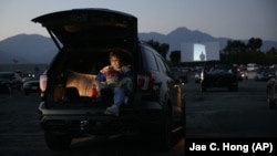 Serena Benavidez looks at her smartphone while waiting for a movie to start at Mission Tiki drive-in theater in Montclair, Calif., on May 28, 2020. (AP Photo/Jae C. Hong, file)