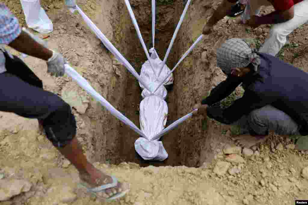 A body of a woman who died from the coronavirus disease (COVID-19), is lowered into the ground during her funeral at a graveyard in New Delhi, India.