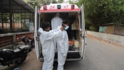 In this file photo, Izhaar Hussain Shaikh, right, an ambulance driver who works for HelpNow, an initiative to help the stretched services of first responders, is assisted by his helper to wear the face mask before picking up a COVID-19 patient in Mumbai, India May 28. (AP)