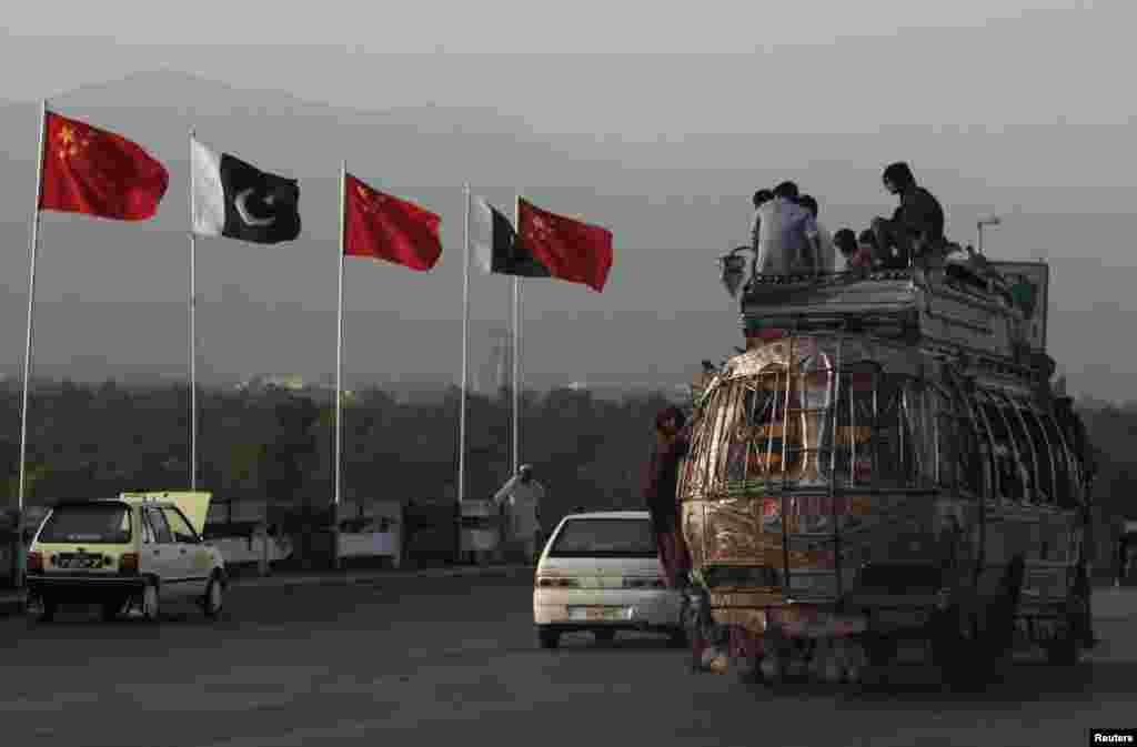People sit on top of a bus as they go past flags of Pakistan and China that are displayed along a road, ahead of Chinese Premier Li Keqiang&#39;s visit to Islamabad.