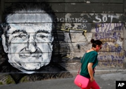 FILE - A woman walks past graffiti on a wall that shows late actor Robin Williams after he was found dead at his home in California, in Belgrade, Serbia, Aug. 13, 2014.