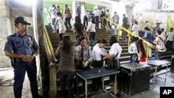 A Filipino policeman stands guard as security guards inspect the bags of passengers at a commuter train station in suburban Manila, Philippines, 26 Jan 2011