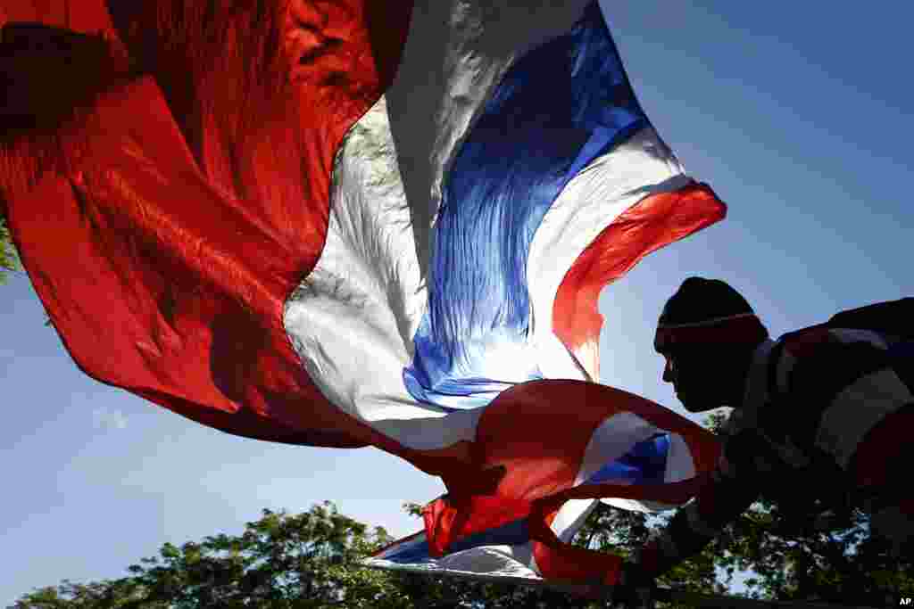 Seorang pengunjuk rasa anti-pemerintah melambaikan bendera nasional Thailand ketika terjadi unjuk rasa di pusat kota Bangkok. Komisi anti korupsi negara itu mendakwa&nbsp; perdana menteri yang digulingkan Yingluck Shinawatra pada hari Kamis atas tuduhan kelalaian dalam tugas mengawasi program subsidi beras yang mendapat kecaman luas. &nbsp;