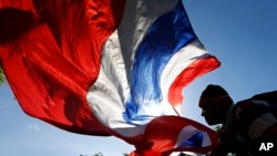 Seorang pengunjuk rasa anti-pemerintah melambaikan bendera nasional Thailand ketika terjadi unjuk rasa di Bangkok. Komisi anti korupsi negara itu mendakwa perdana menteri yang digulingkan Yingluck Shinawatra atas tuduhan kelalaian dalam tugas mengawasi program subsidi beras yang mendapat kecaman luas.
