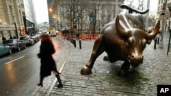 FILE - People pass the statue of the bull near Wall Street in New York.