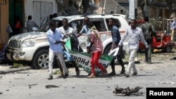 Civilians carry the dead body of a man killed in a car bomb explosion near a hotel in Mogadishu, Somalia, March 28, 2019. 