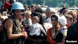 Žene i deca, uz pripadnika holandskog bataljona UN, čekaju na transportovanje iz Potočara; 12. jul 1995.