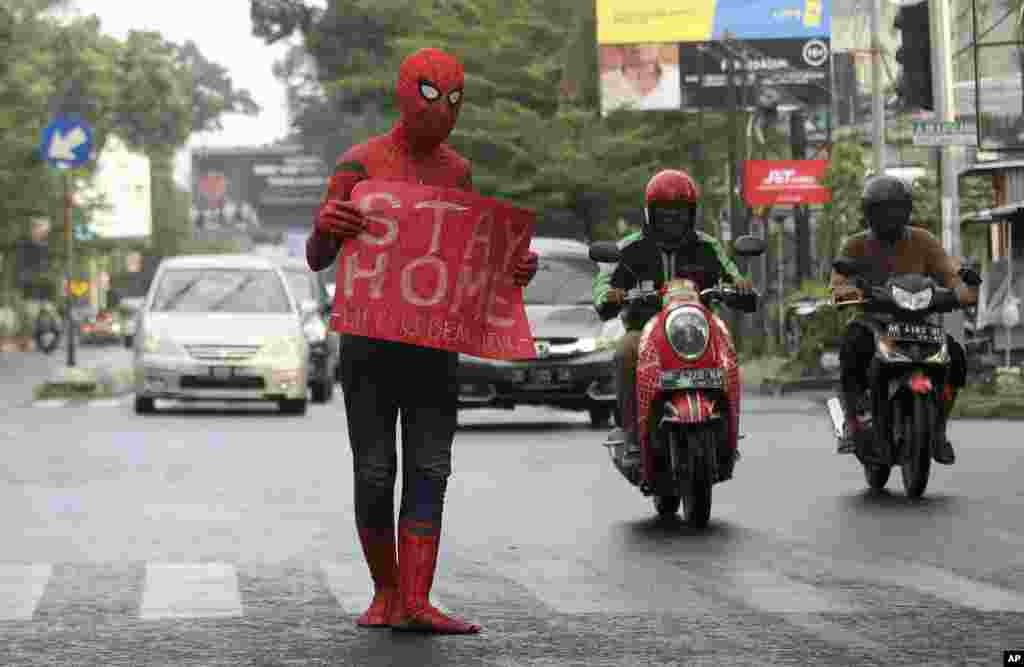 یک مرد در لباس اسپایدرمن با پوستری که بر روی نوشته: &laquo;در خانه بمانید&raquo;، سعی در آگاهی رساندن به شهروندان در ماکاسار، اندونزی، دارد.