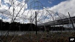 FILE - Razor wire recently placed by the U.S.military along the banks of the Rio Grande frames the McAllen-Hidalgo International Bridge at the U.S.-Mexico border, Nov. 3, 2018, in McAllen, Texas.