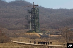FILE - A group of journalists walk down a road in front of North Korea's Unha-3 rocket at the Sohae Satellite Station in Tongchang-ri, North Korea, April 8, 2012.