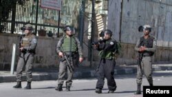 FILE - An Israeli border policeman aims his weapon towards Palestinian protesters as others take up position during clashes in the West Bank city of Bethlehem, Jan. 22, 2016.