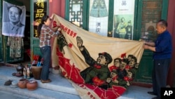 Vendors unfurl a banner from 1969 depicting former Chinese leader Mao Zedong as he "inspects the great army of the Cultural Revolution" and the slogan "Navigating the seas depends on the helmsman" at a curio market in Beijing, China, May 16, 2016. 