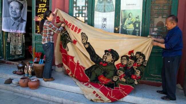 北京旧货市场上的1969年的文革横幅画布，上面有戴红卫兵袖章的毛泽东、其他文革领导人和红卫兵。横幅上写着“大海航行靠舵手” 和“毛主席检阅文化革命大军”（2016年5月16日）