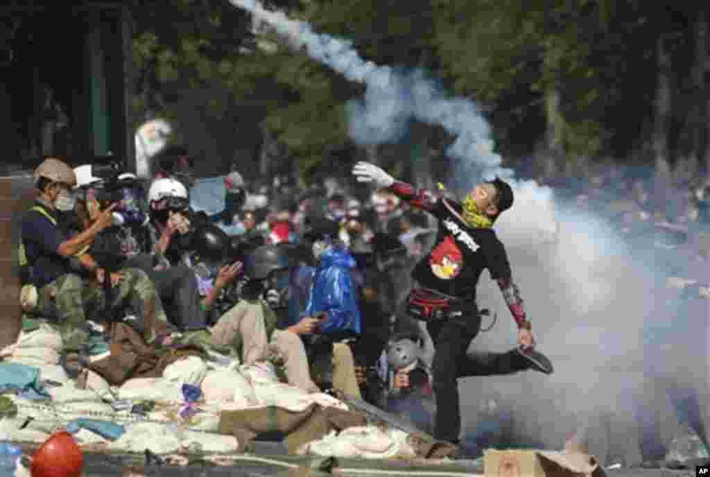 An anti-government protester throws tear gas back to riot police near the Government House in Bangkok, Monday, Dec. 2, 2013. Thailand's Prime Minister Yingluck Shinawatra on Monday rejected the demands of anti-government protesters locked in street battle