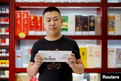 FILE - Shan Yuliang, salesperson at a cigarette and wine shop, poses with a carton of Marlboro cigarettes in Beijing, China, April 8, 2018.