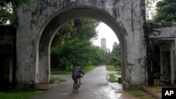 FILE - A woman rides a bicycle through the entrance gate of Yangon University in Yangon, Myanmar, June 28, 2012.