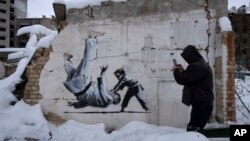 A man takes a photo of an artwork that was made by British street artist Banksy on a building destroyed by the Russian army in Borodyanka, Kyiv region, Ukraine, Dec. 6, 2022. 