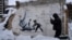 A man takes a photo of an artwork that was made by British street artist Banksy on a building destroyed by the Russian army in Borodyanka, Kyiv region, Ukraine, Dec. 6, 2022. 