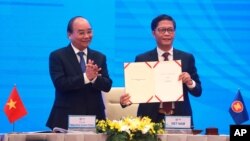 Vietnamese Prime Minister Nguyen Xuan Phuc, left, applauds as Minister of Trade Tran Tuan Anh, right, holds up a signed document during a virtual signing ceremony of the Regional Comprehensive Economic Partnership, or RCEP, trade agreement in Hanoi.