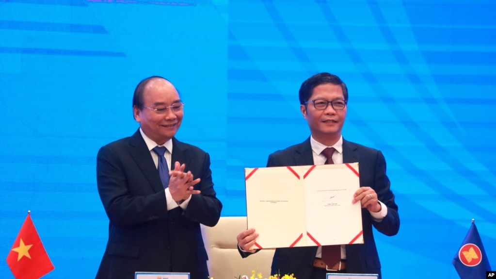 Vietnamese Prime Minister Nguyen Xuan Phuc, left, applauds as Minister of Trade Tran Tuan Anh, right, holds up a signed document during a virtual signing ceremony of the Regional Comprehensive Economic Partnership, or RCEP, trade agreement in Hanoi…
