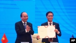 Vietnamese Prime Minister Nguyen Xuan Phuc, left, applauds as Minister of Trade Tran Tuan Anh, right, holds up a signed document during a virtual signing ceremony of the Regional Comprehensive Economic Partnership, or RCEP, trade agreement in Hanoi…