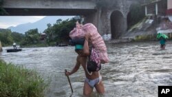 Men carry loads of supplies as they cross the Suchiate river from Guatemala into Talisman, Mexico, June 21, 2019. Mexico's foreign minister says that the country has completed its deployment of some 6,000 National Guard members to help.
