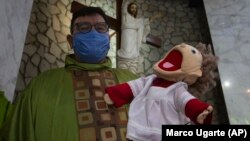 Pendeta Katolik Carlos Cardona berpose dengan bonekanya Monsi, seorang putra altar, di gereja Saint Judas Thaddeus di Huixquilucan, Mexico City, Minggu, 27 Juni 2021. (Foto: AP/Marco Ugarte)