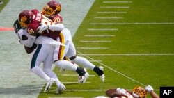 Washington Football Team defensive end Montez Sweat (90) falls while tearing a piece of of Philadelphia Eagles running back Jason Huntley's jersey who is being tackled by Washington Football Team strong safety Landon Collins (26) and cornerback Jimmy Moreland (20) during the first half of an NFL football game, Sept. 13, 2020, in Landover, Maryland. 
