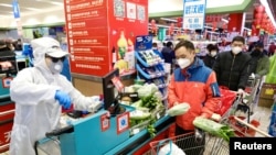 Prodavac u zaštitnoj odjeći uslužuje kupce na kasi supermarketa, u Wuhanu, pokrajina Hubei, Kina, 12. februara 2020. (PHOTO: China Daily via REUTERS)
