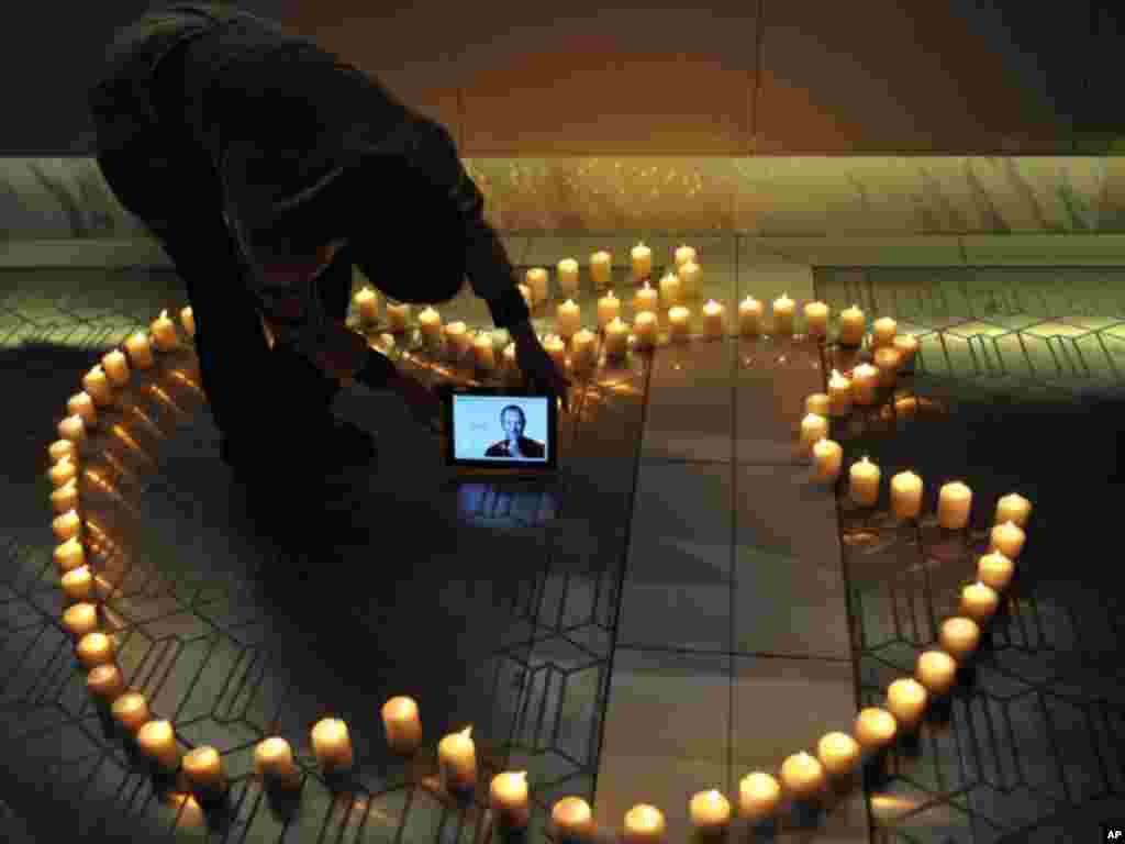 A man places an iPad displaying a picture of Steve Jobs around candles forming the logo of Apple Inc., the company he co-founded, in Chengdu in southwestern China's Sichuan province, on Thursday, Oct. 6, 2011.