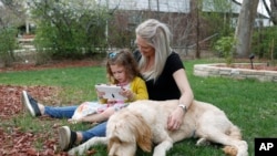 Katie Evers, who is facing the specter of paying the monthly rent with the flip of the calendar, helps her 4-year-old daughter, Everlee, read a tablet while their goldendoodle lies next to them outside their home in southeast Denver, April 30, 2020. 