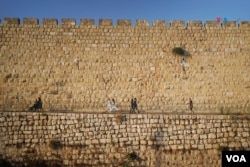 Varias personas caminan junto a la muralla que rodea la Ciudad Vieja de Jerusalén.