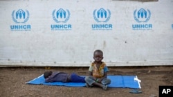 (FILE) In this June 9, 2017, file photo, a South Sudanese refugee boy sits on a mat outside a communal tent while his brother sleeps, at the Imvepi reception center in northern Uganda.