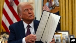 FILE - President Donald Trump holds up a signed executive order in the Oval Office of the White House, in Washington, Jan. 23, 2025.