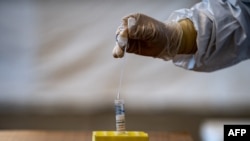 FILE - A lab technician wearing protective gear puts a swab into a container during a demonstration of a swab test for the COVID-19 virus, in Tokyo, Japan, May 8, 2020.