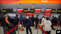 FILE- Travelers wearing face masks wait in line at the Hainan Airlines check-in counters at Beijing Capital International Airport in Beijing, March 6, 2020.