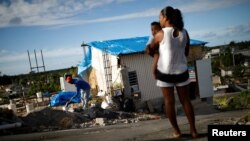 FILE - Samuel Vasquez rebuilds his house, which was partially destroyed by Hurricane Maria, while his wife Ysamar Figueroa looks on, whilst carrying their son Saniel, at the squatter community of Villa Hugo in Canovanas, Puerto Rico, Dec. 11, 2017. Villa Hugo is a settlement initially formed by people whose houses were damaged or destroyed by Hurricane Hugo in 1989. 