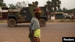 FILE - A woman walks past French peacekeeping soldiers patrolling in an armored vehicle, following continuing sectarian violence in the capital, Bangui, on Feb. 4, 2014.
