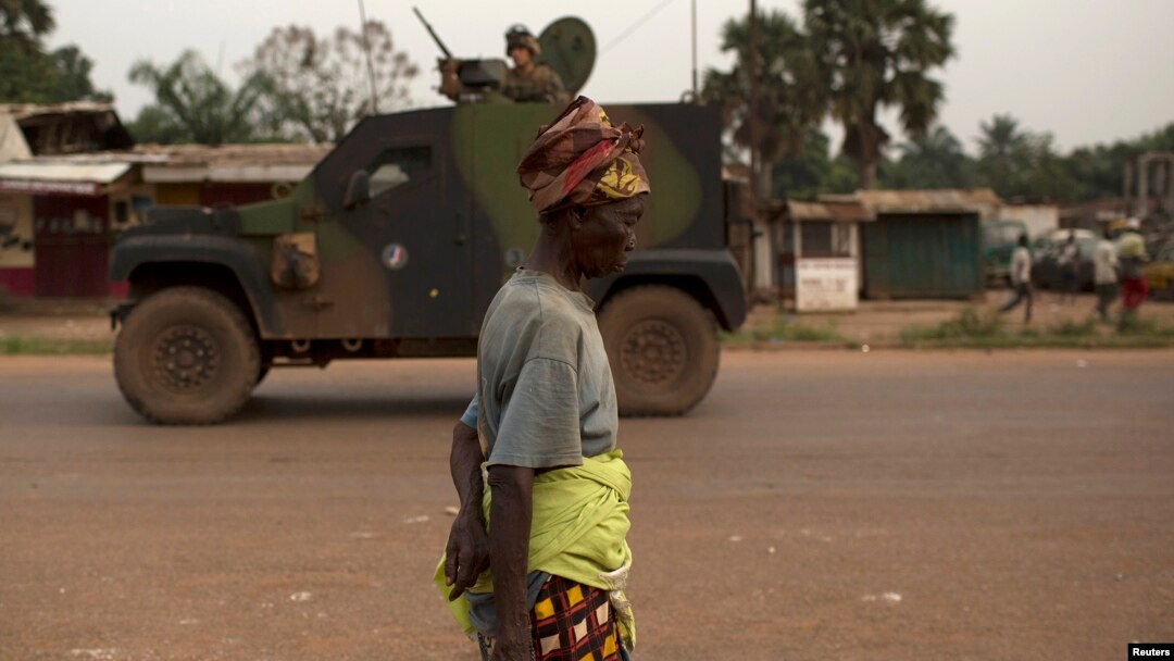 FILE - A woman walks past French peacekeeping soldiers patrolling in an armored vehicle, following continuing sectarian violence in the capital, Bangui, on Feb. 4, 2014.